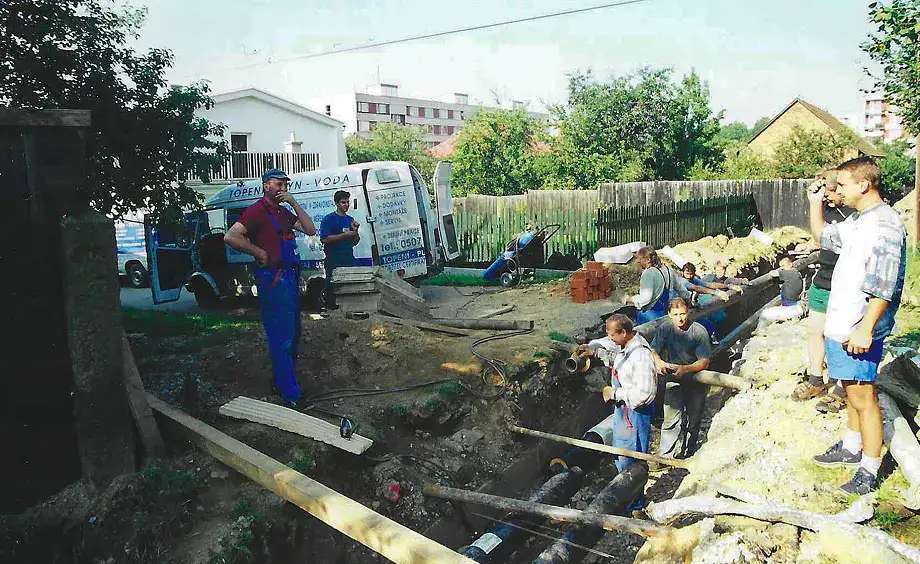 Děti a pracovníci na staveništi při výkopových pracích.
