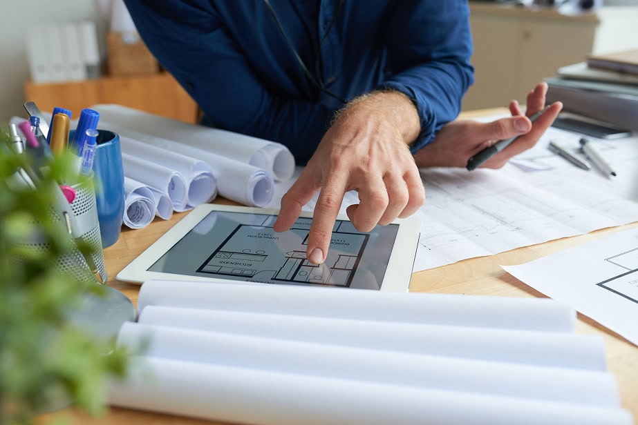 Osoba pracující na projektech staveb s tabletem a plány.