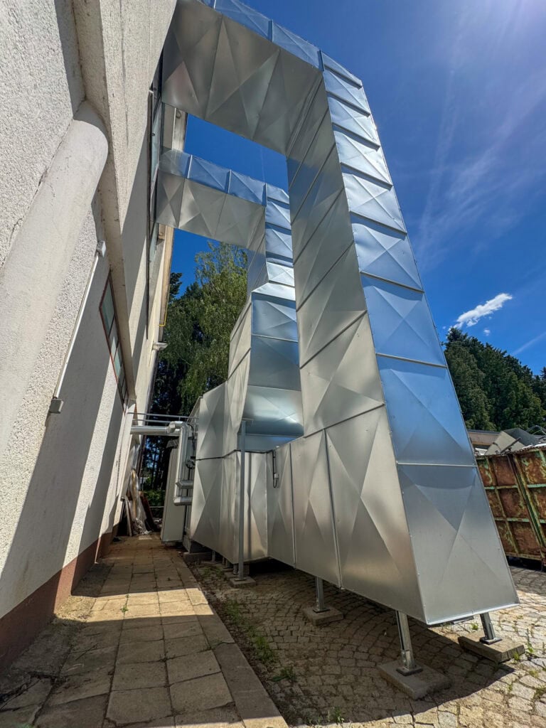 Moderní průmyslová ventilace s kovovými potrubími na střeše budovy.